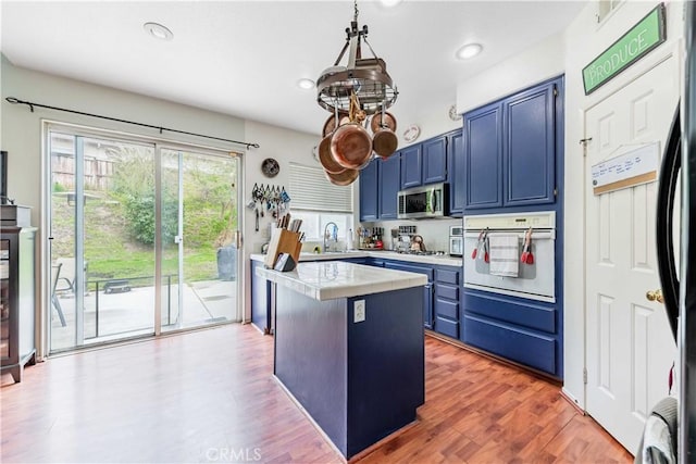 kitchen with a center island, blue cabinetry, light countertops, stainless steel microwave, and oven