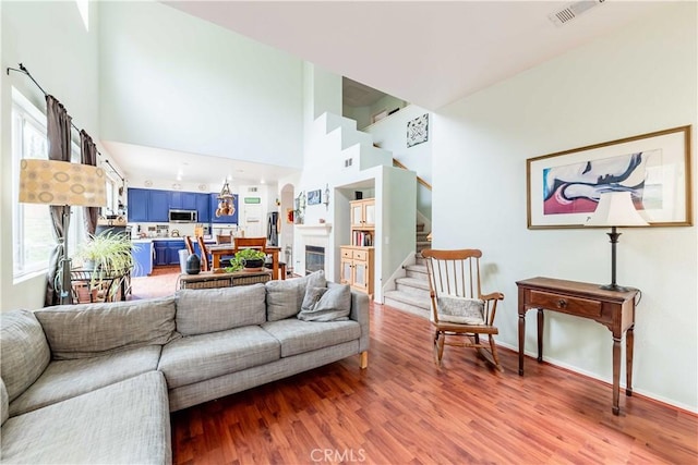 living room featuring visible vents, stairway, a high ceiling, a glass covered fireplace, and wood finished floors