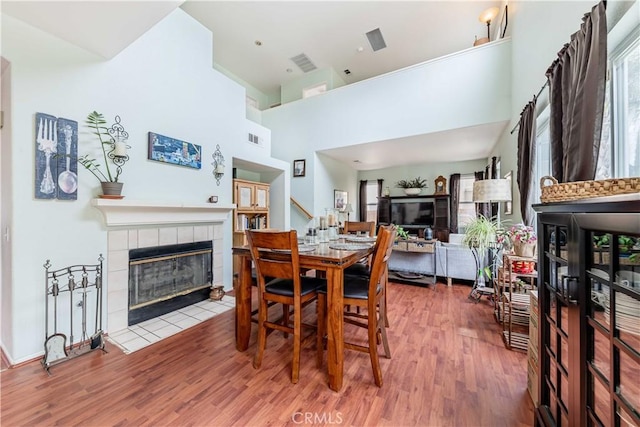 dining area featuring a tile fireplace, visible vents, stairway, and wood finished floors