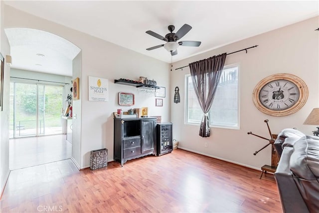 interior space with light wood-type flooring, ceiling fan, arched walkways, and baseboards