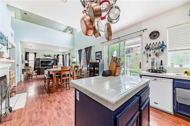 kitchen with a fireplace, tile countertops, blue cabinets, light wood-type flooring, and dishwasher