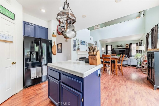 kitchen with tile counters, open floor plan, blue cabinets, light wood-type flooring, and black fridge