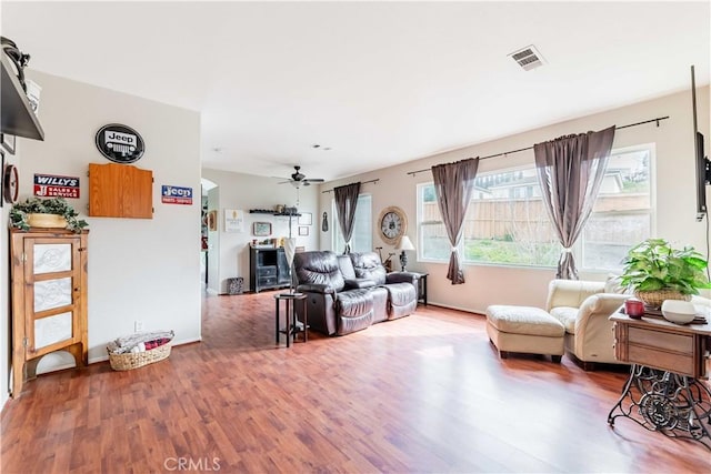 living area with ceiling fan, wood finished floors, visible vents, and baseboards