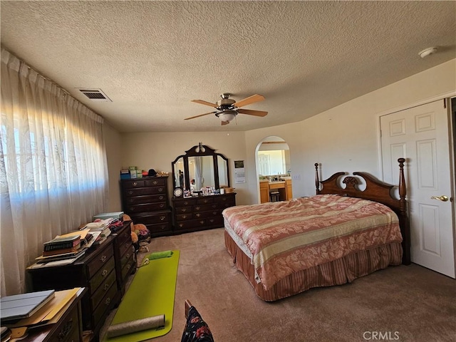 bedroom featuring arched walkways, visible vents, light carpet, ceiling fan, and a textured ceiling