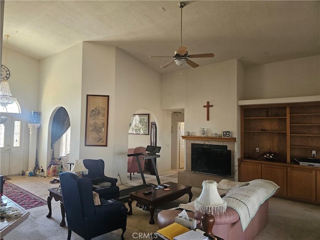 living room with arched walkways, a tiled fireplace, carpet flooring, ceiling fan, and a textured ceiling