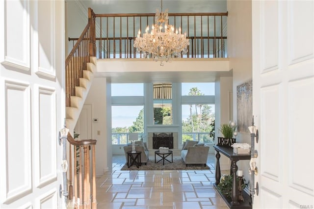 entryway featuring a notable chandelier, stone tile flooring, a fireplace with raised hearth, stairway, and a high ceiling