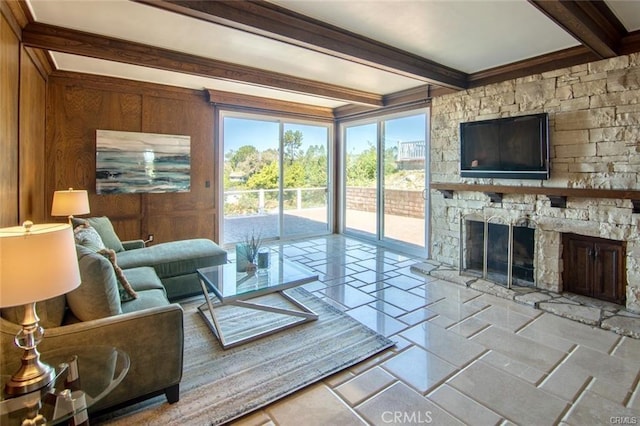 living area with a stone fireplace, wood walls, beam ceiling, and stone tile flooring