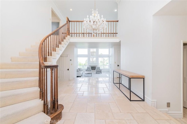 entryway with a notable chandelier, stairway, a towering ceiling, stone finish flooring, and baseboards