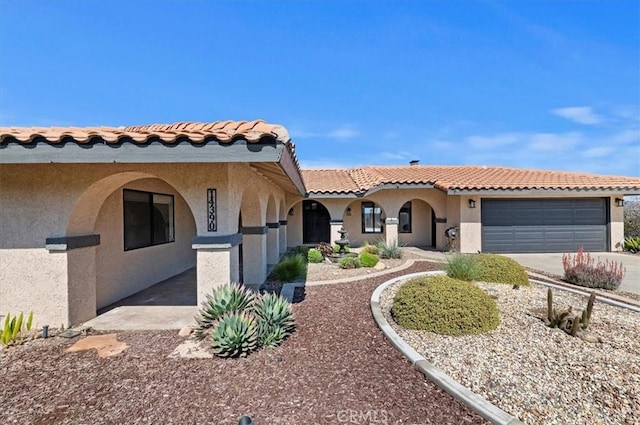 mediterranean / spanish house with a garage, driveway, a tile roof, and stucco siding