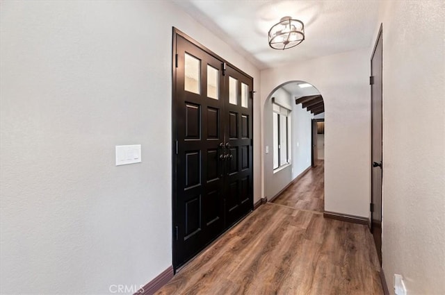 entryway featuring arched walkways, wood finished floors, and baseboards