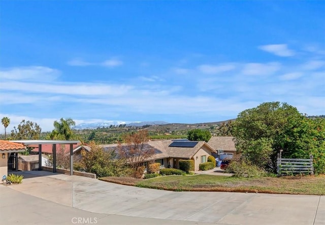 view of front of house with driveway, solar panels, a tile roof, fence, and a mountain view