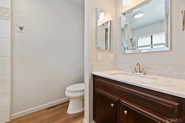 bathroom featuring baseboards, tiled shower, toilet, wood finished floors, and vanity