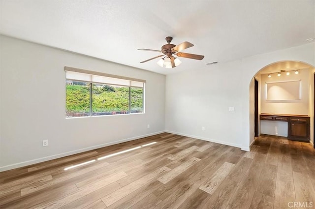 unfurnished room featuring arched walkways, visible vents, baseboards, and wood finished floors