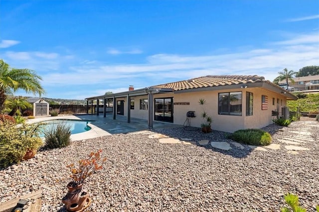 back of house featuring an outbuilding, stucco siding, a patio area, a shed, and a tiled roof