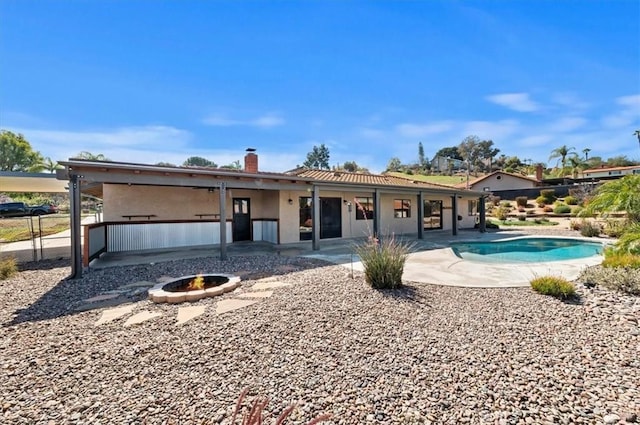 back of property with a patio, a fire pit, fence, an outdoor pool, and a chimney