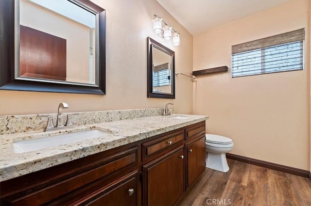 bathroom featuring double vanity, a sink, toilet, and wood finished floors