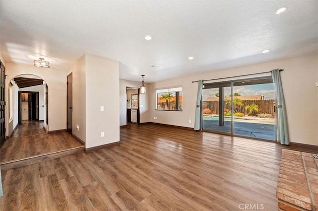 unfurnished living room with baseboards, arched walkways, wood finished floors, and recessed lighting