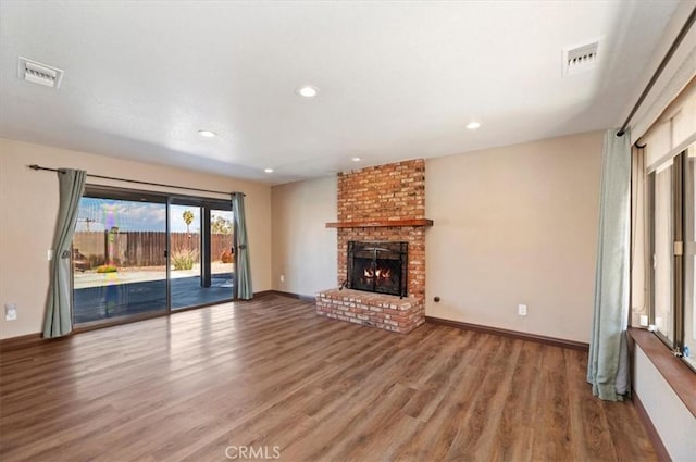 unfurnished living room with visible vents, a fireplace, baseboards, and wood finished floors