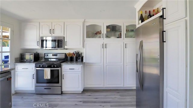 kitchen with white cabinetry, light stone countertops, light wood-style floors, and stainless steel appliances