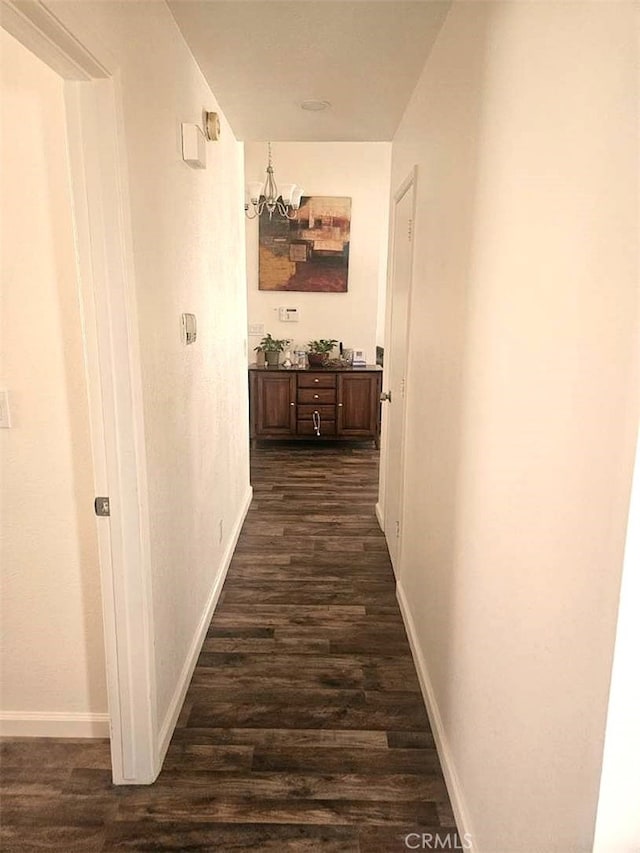 hallway featuring dark wood-style flooring, baseboards, and an inviting chandelier