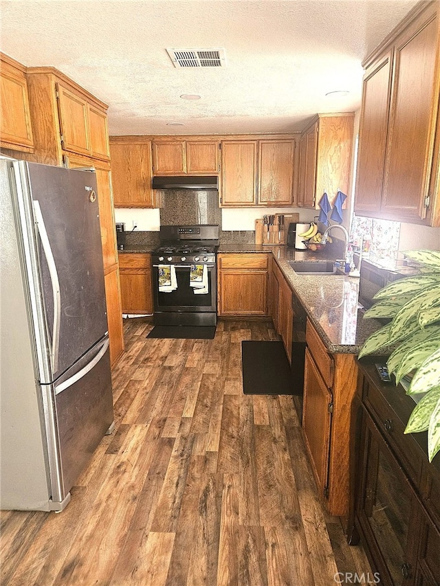 kitchen featuring under cabinet range hood, dark wood-type flooring, a sink, visible vents, and appliances with stainless steel finishes