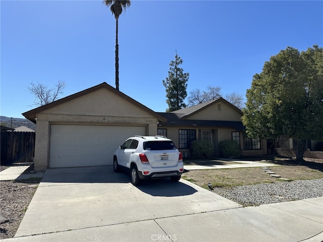 ranch-style house featuring an attached garage, fence, concrete driveway, and stucco siding