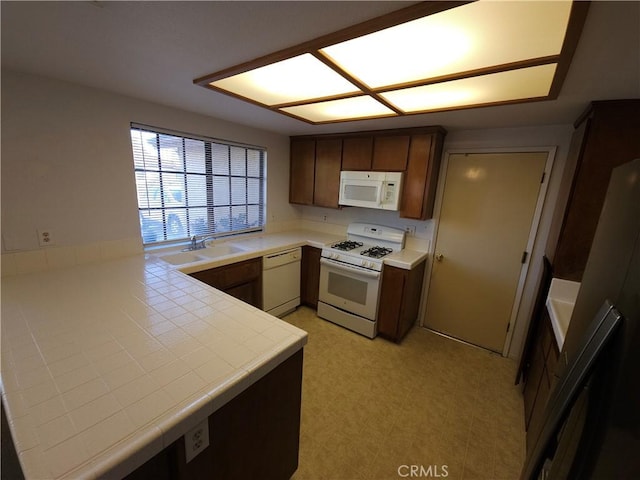 kitchen with tile countertops, light floors, a sink, white appliances, and a peninsula