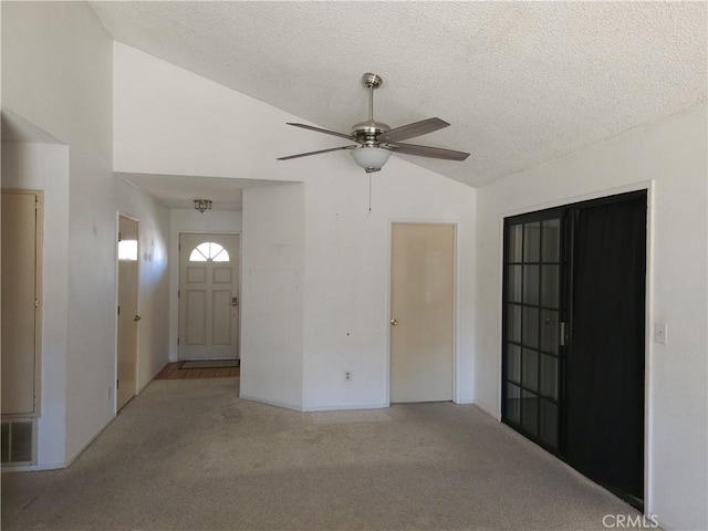 carpeted entryway with visible vents, vaulted ceiling, a textured ceiling, and ceiling fan