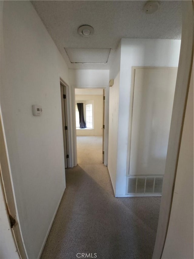 hallway featuring a textured ceiling, carpet floors, attic access, and baseboards