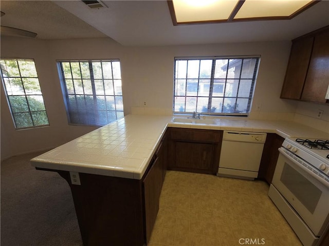 kitchen with tile countertops, white appliances, plenty of natural light, and a sink