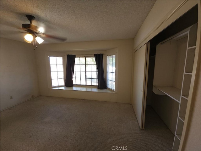 unfurnished bedroom with a textured ceiling, carpet floors, a closet, and ceiling fan