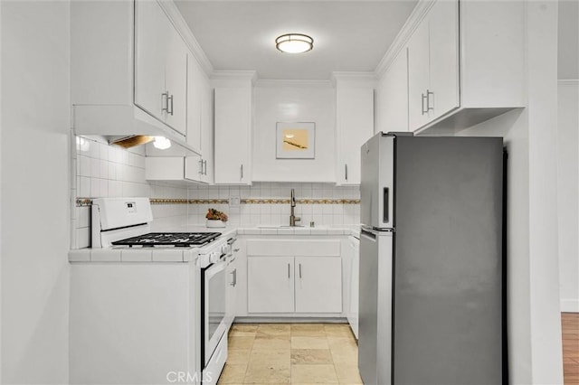 kitchen with tile countertops, white range with gas stovetop, freestanding refrigerator, a sink, and under cabinet range hood