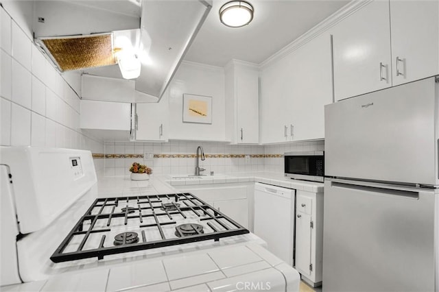 kitchen with stainless steel microwave, tile counters, dishwasher, freestanding refrigerator, and a sink