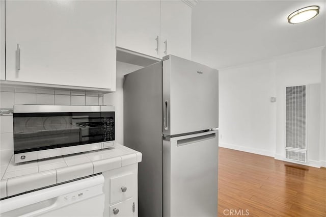 kitchen featuring white cabinetry, tile countertops, appliances with stainless steel finishes, light wood finished floors, and a heating unit