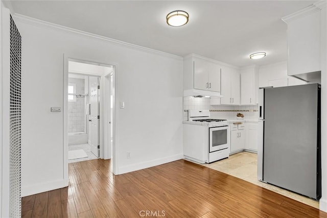 kitchen with under cabinet range hood, white gas stove, freestanding refrigerator, and ornamental molding