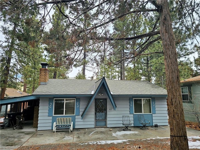 view of front facade featuring a carport, a chimney, and a shingled roof