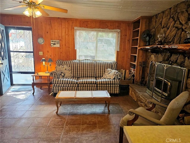 living room with wooden walls, ceiling fan, built in features, a stone fireplace, and wooden ceiling