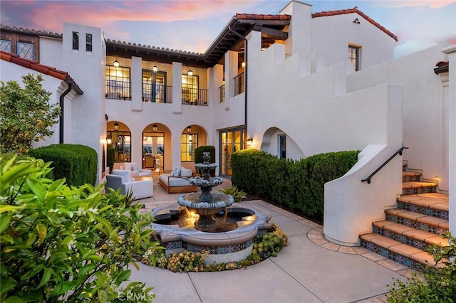 back of property at dusk featuring stucco siding, a balcony, a patio area, and a tiled roof