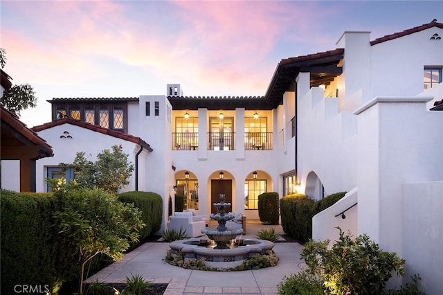 rear view of property featuring stucco siding, a balcony, and a tile roof