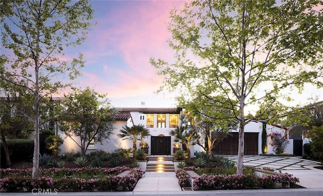 view of front facade featuring a tiled roof, a garage, driveway, and stucco siding