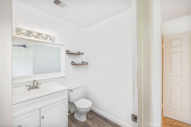 bathroom featuring visible vents, baseboards, toilet, wood finished floors, and vanity