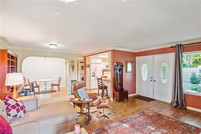 foyer with stacked washer / dryer, crown molding, arched walkways, and wood finished floors