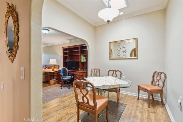 dining room featuring ornamental molding, baseboards, arched walkways, and light wood-style floors