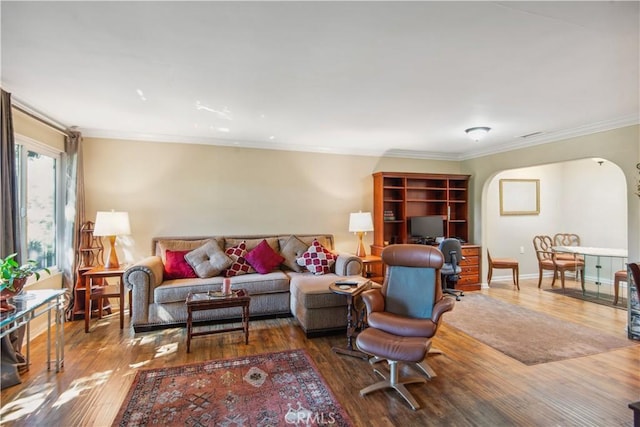 living area with ornamental molding, arched walkways, and wood finished floors