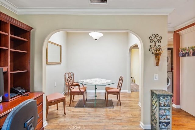 dining space featuring light wood-style flooring, stacked washer and dryer, arched walkways, and visible vents