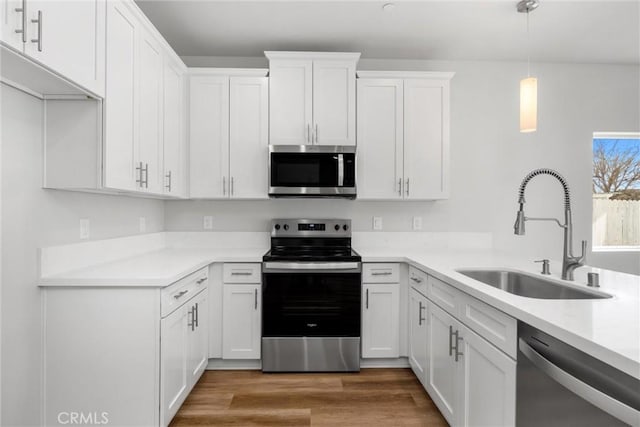 kitchen featuring light countertops, appliances with stainless steel finishes, white cabinets, a sink, and wood finished floors