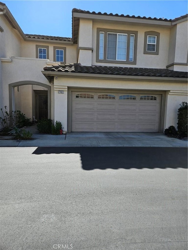 townhome / multi-family property featuring an attached garage, a tiled roof, concrete driveway, and stucco siding