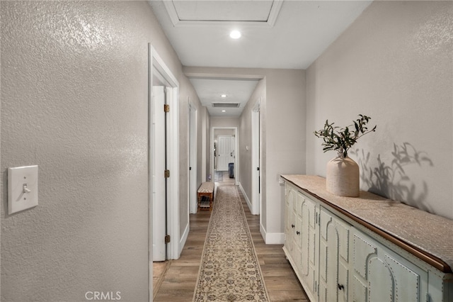 hall with visible vents, baseboards, attic access, light wood-style flooring, and a textured wall