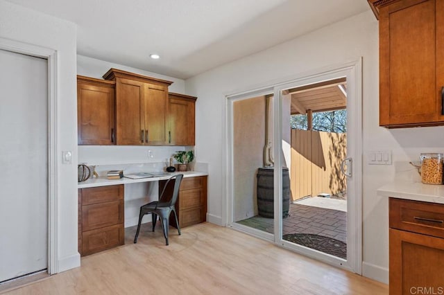 kitchen featuring brown cabinetry, baseboards, light wood-style flooring, light countertops, and built in desk