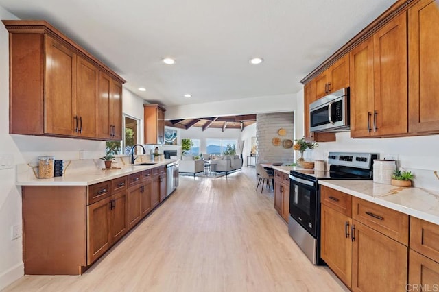 kitchen with brown cabinetry, light wood-type flooring, a sink, appliances with stainless steel finishes, and open floor plan